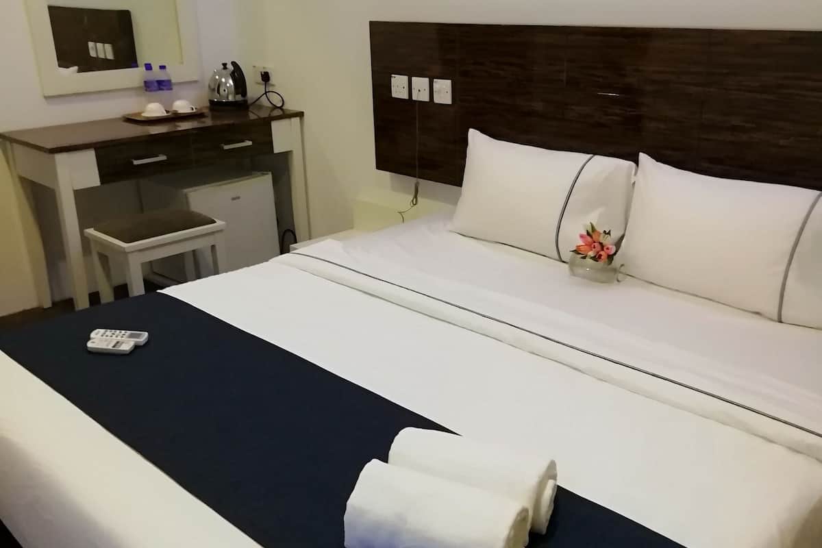 A hotel room with a bed, a desk, a chair, and a small table with a kettle and cups.