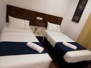 A hotel room with two beds, each with a blue bedspread and white linens, a wooden headboard, a bedside table with a phone and a vase of flowers, and a wall-mounted artwork. - Hotel Fujisan PWTC (Kuala Lumpur)