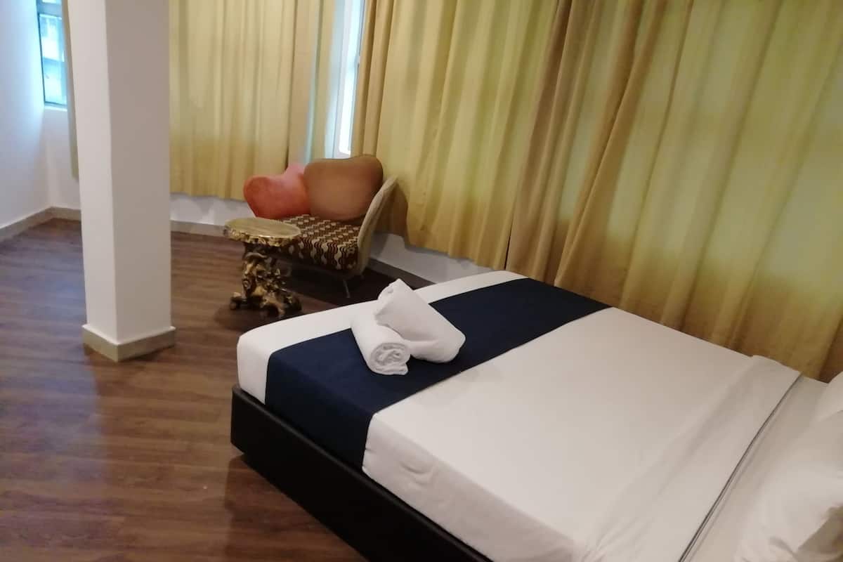 A hotel room with a neatly made bed, a small round table with a chair, and a window with curtains.