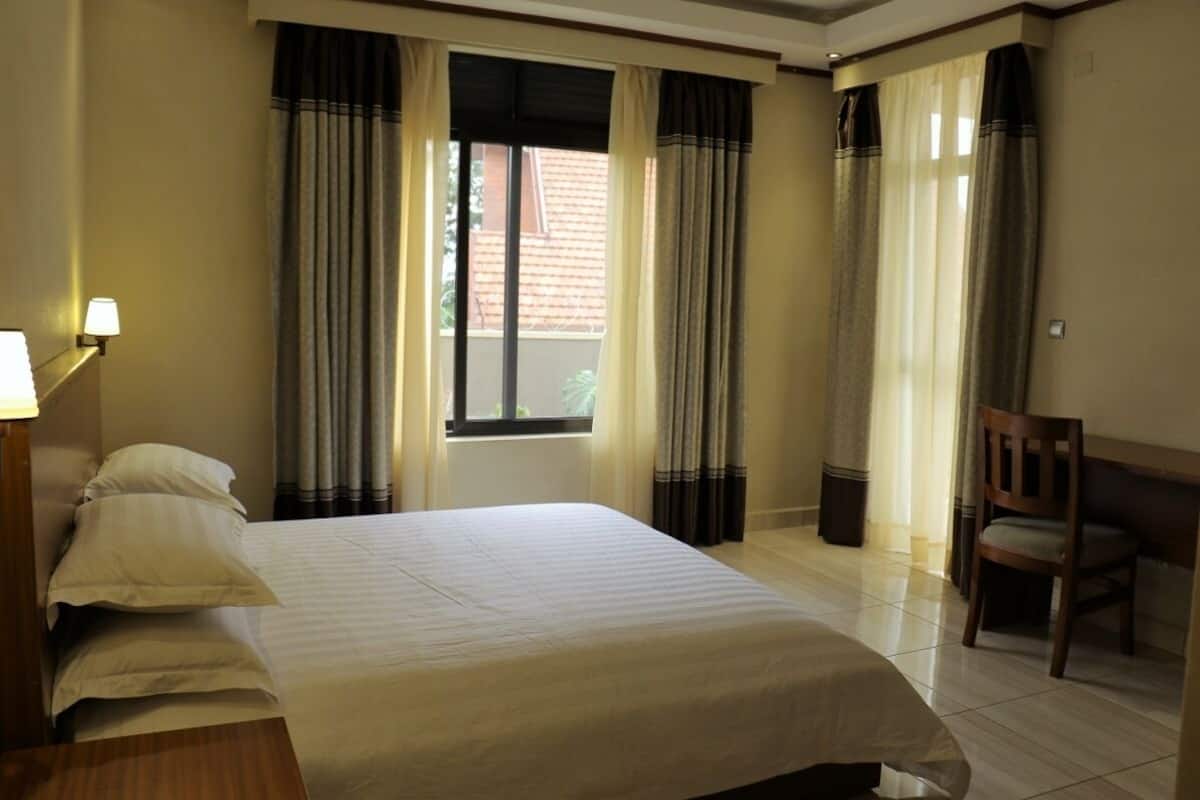 A hotel room with a bed, a chair, a desk, and a window with curtains.