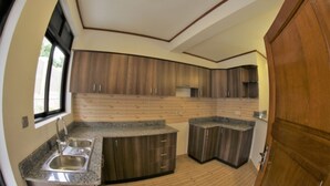 A compact kitchen with wooden cabinets, granite countertops, and a built-in sink. - Nandi Residence (Kigali)
