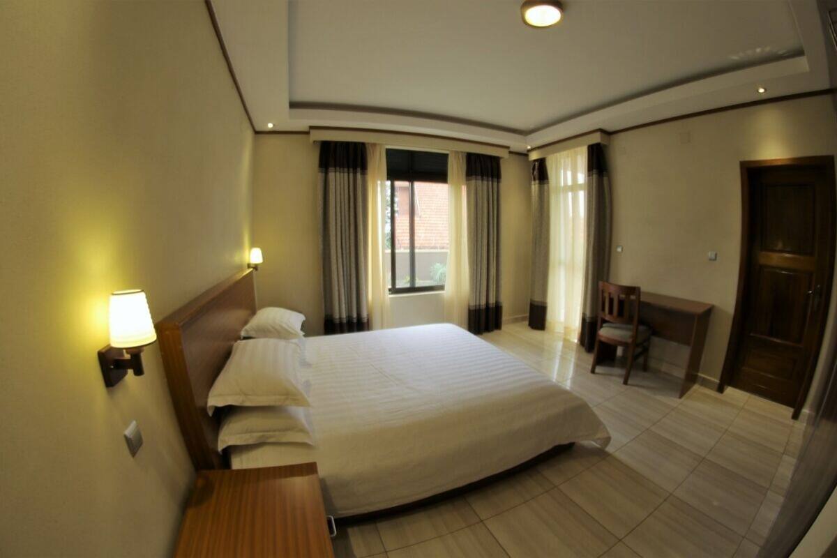 A hotel room with a large bed, a desk, a chair, a window with curtains, and a door.