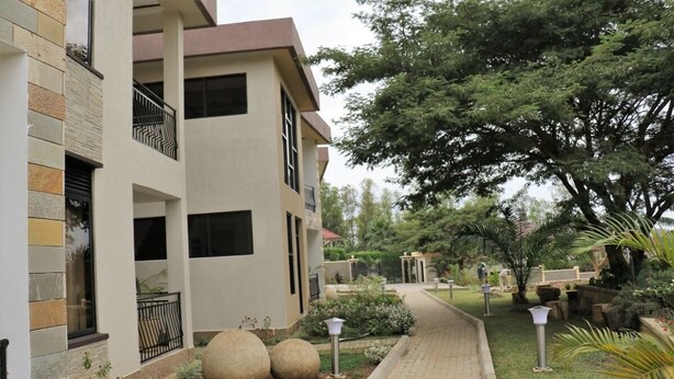 A modern building with a multi-story structure, a paved walkway, and landscaped gardens with large decorative stones and trees. - Nandi Residence (Kigali)