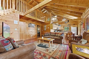A log cabin interior with a living room, kitchen, and dining area.