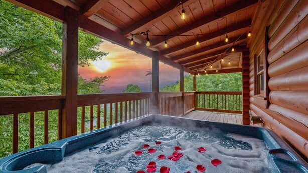 A hot tub with rose petals on a wooden deck with a sunset view.