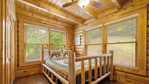 A wooden cabin room with a bed, large windows, and a ceiling fan.