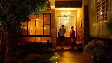 A modern building with a well-lit entrance, a visible staircase, and a small garden area with a bench and potted plants.
