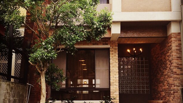 A modern building with a brick facade, large windows, and a well-maintained garden with a tree and rocks. - Lin's Inn (Ruisui)