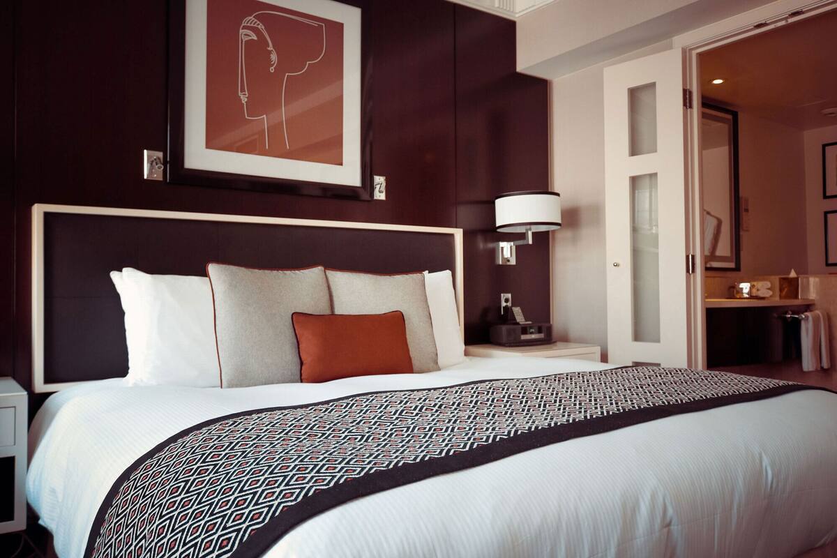 Habitación de hotel con una cama grande, un cabecero, una mesita de noche con lámpara y un cuadro en la pared.