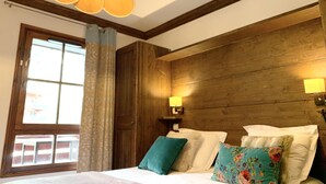 A bedroom with a wooden headboard, a large window with curtains, and a bed with multiple pillows.