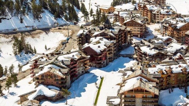 A snow-covered resort with multiple buildings, a central pool, and surrounding trees.