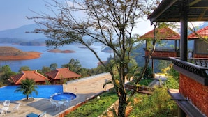 A resort with a swimming pool, red-roofed buildings, and a view of a lake and mountains. - Contour Island Resort & Spa (Vythiri)