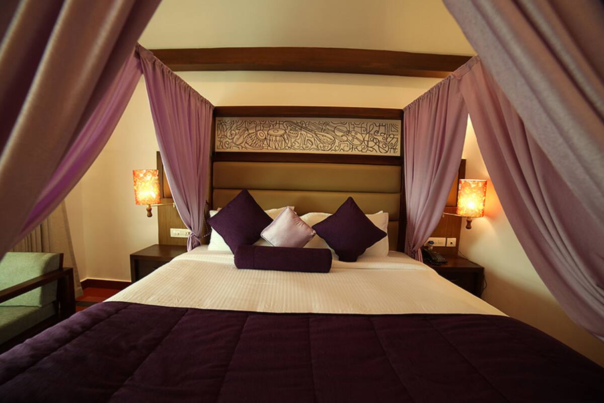 A hotel room with a large bed, purple curtains, and two bedside lamps.