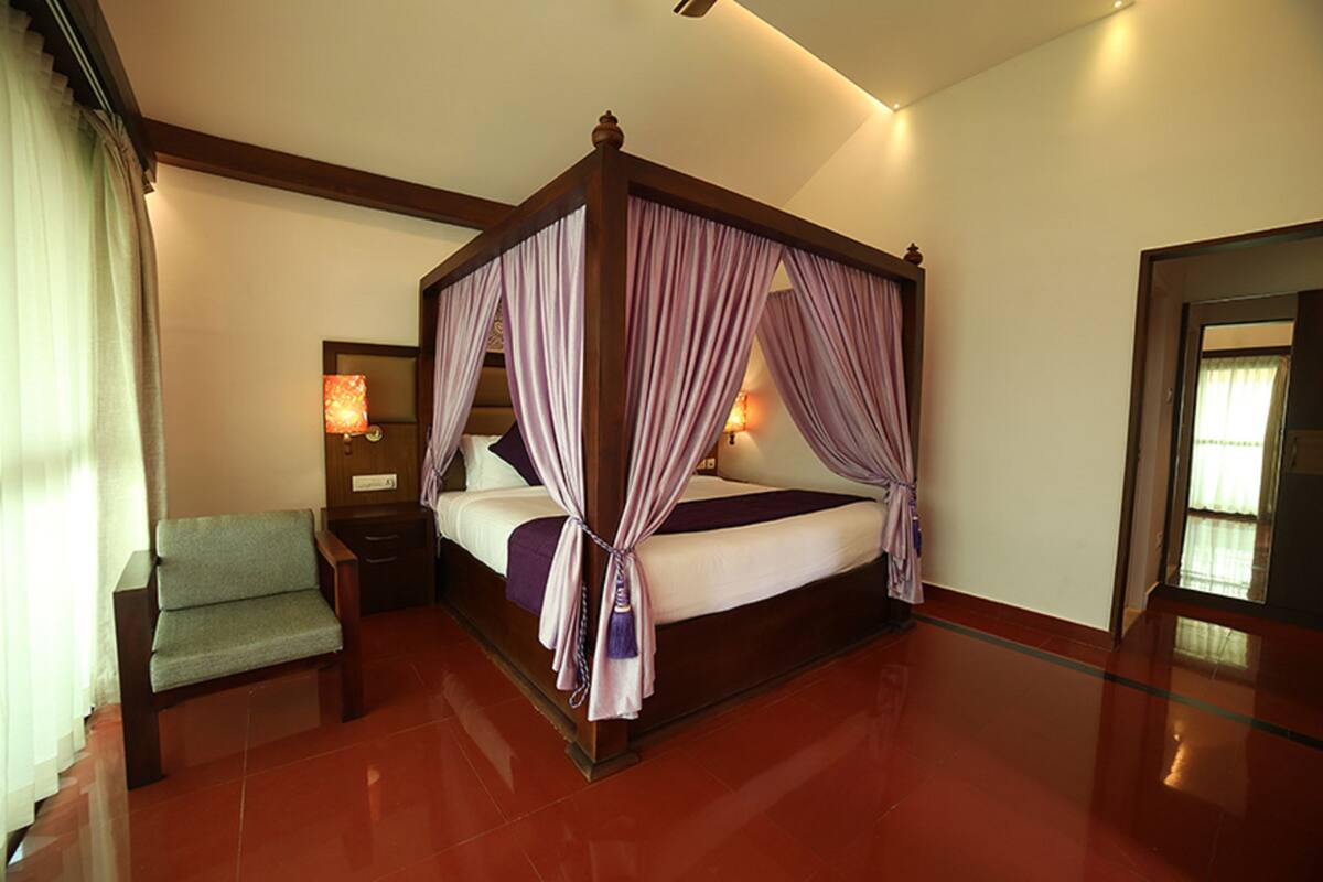 A four-poster bed with curtains, a nightstand, a chair, and a lamp.