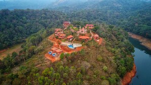 An aerial view of a resort with multiple red-roofed buildings, a swimming pool, and a river nearby. - Contour Island Resort & Spa (Vythiri)