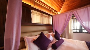 A bedroom with a bed, purple pillows, and a wooden ceiling. - Contour Island Resort & Spa (Vythiri)