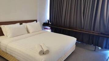 A neatly made bed with white linens and a rolled towel, a wooden headboard, and a small table with a lamp.