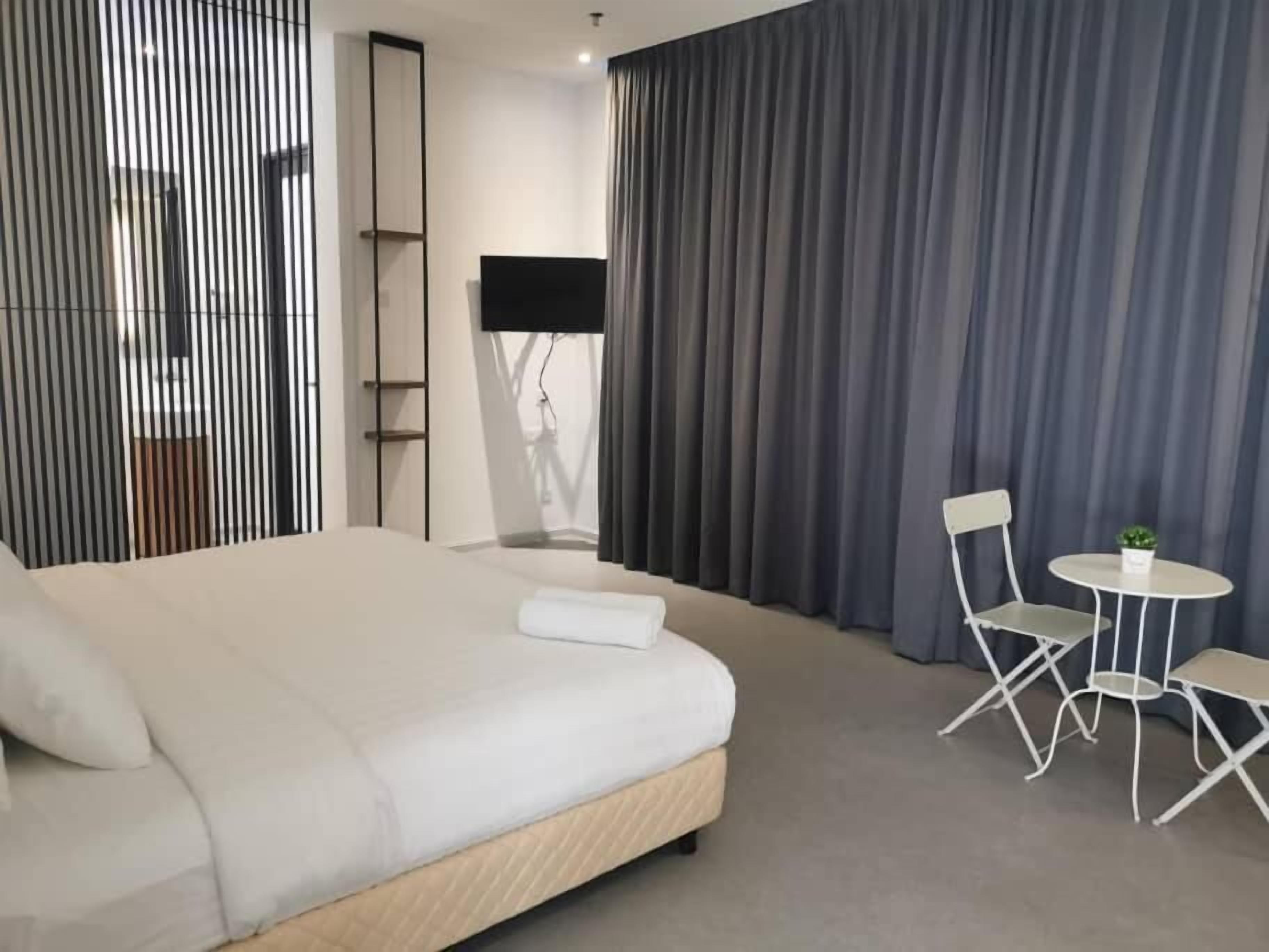 Une chambre d’hôtel moderne avec un grand lit, une petite table avec deux chaises, une télévision et une fenêtre avec des rideaux.