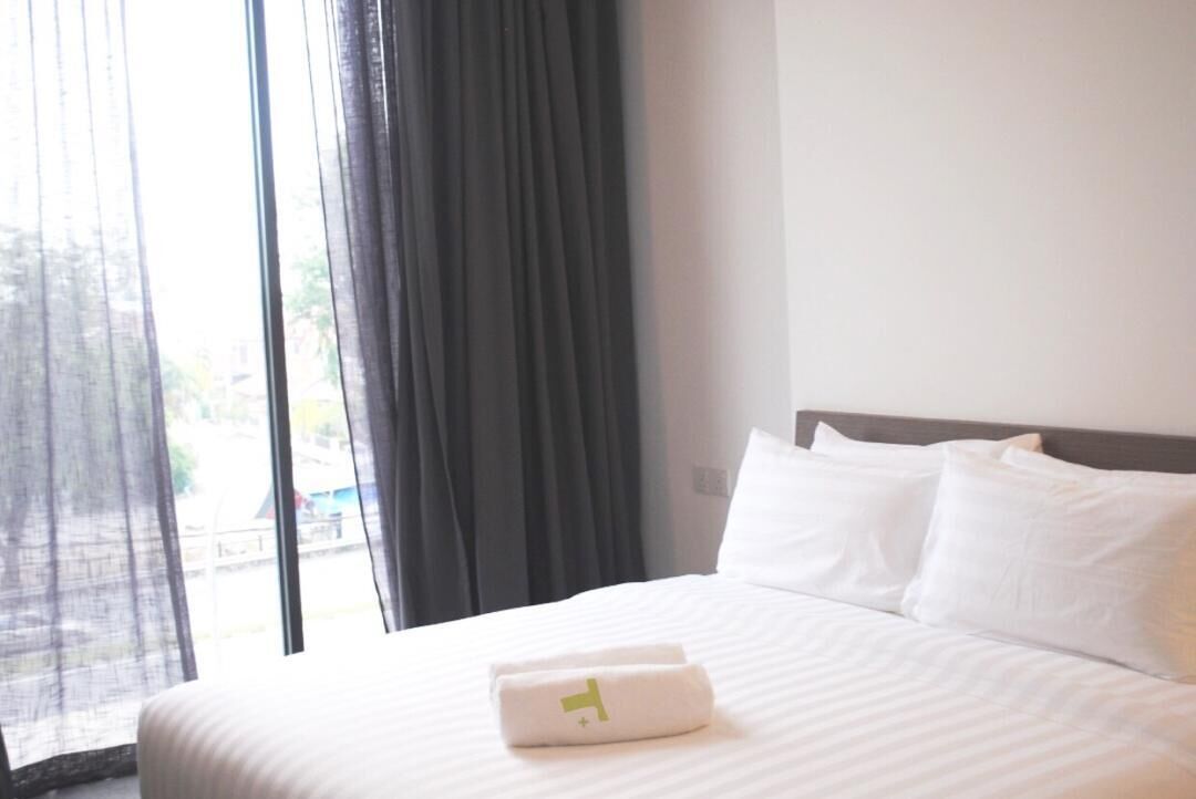 A hotel room with a large bed, white bedding, and a window with sheer curtains.