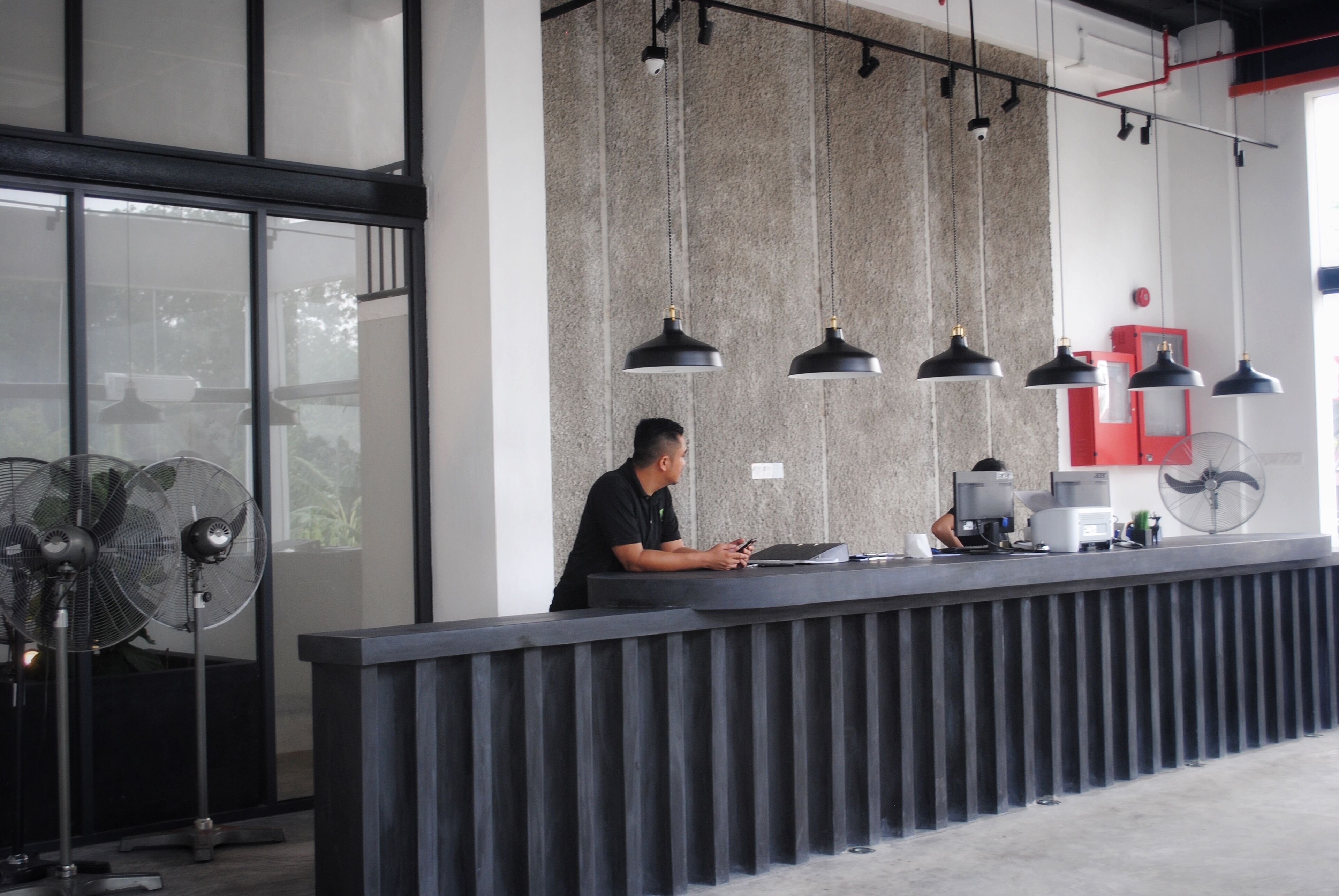 A reception desk with a modern design, featuring a black countertop, multiple black pendant lights, and a large window providing natural light.