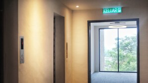 A hallway with a sign reading "KELUAR" leading to a door with a view of trees outside. - T+ Premium Hotel (Alor Setar)