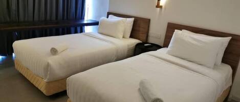 A hotel room with two single beds, each with a pillow and a rolled towel.