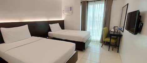 A hotel room with two beds, a desk with a chair, a television, and a window with curtains.