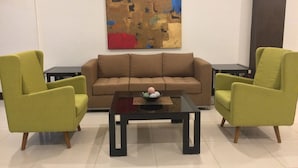 Una sala de estar moderna con un sofá marrón, dos sillones verdes y una mesa de centro negra.