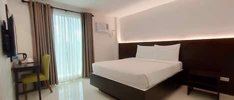 A hotel room with a bed, a desk, a chair, a TV, and a window with curtains.