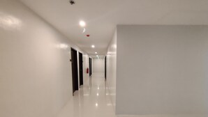 Un pasillo largo y estrecho con paredes blancas y piso brillante que conduce a una puerta al final.