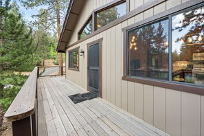 A wooden deck with a metal railing, a door, and a window overlooking a forested area.