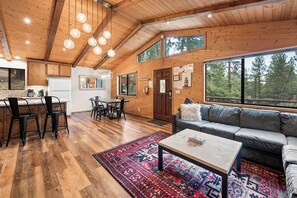 A spacious living area with a wooden ceiling, a dining table with chairs, a sofa, and a coffee table.