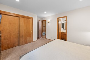 A bedroom with a large bed, wooden wardrobe, and a bathroom with a mirror and sink.