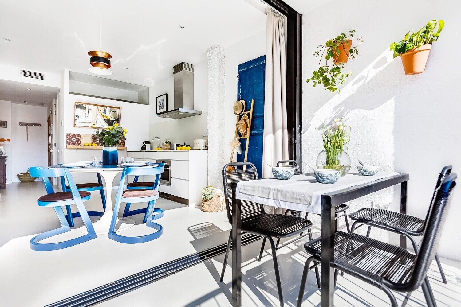 Una cocina moderna con armarios blancos, una puerta azul y un comedor con sillas negras y una mesa blanca.
