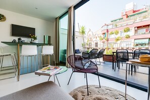 Un salon moderne doté d’une grande fenêtre, d’un téléviseur à écran plat et d’un coin repas avec des chaises et une table.