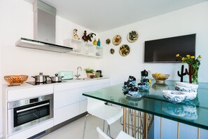 A modern kitchen with white cabinets, a Bosch oven, a glass table, and decorative plates on the wall.