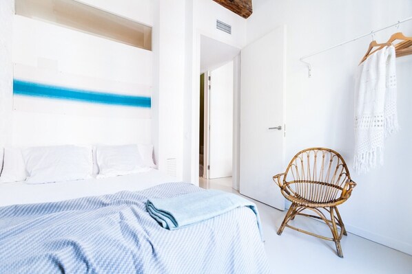 A bedroom with a bed, a wicker chair, a white wardrobe, and a blue wall accent.
