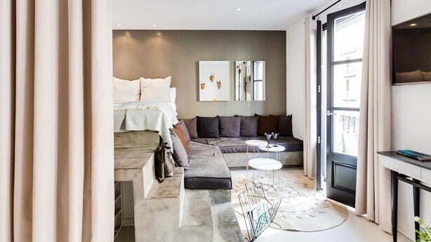Ein modernes, helles Zimmer mit einem Bett, einer Couch, einem kleinen Tisch und einem Fernseher.