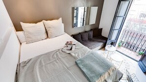 Ein modernes Schlafzimmer mit einem großen Bett, einem Sofa, einem kleinen Tisch und einem Balkon mit Blick.