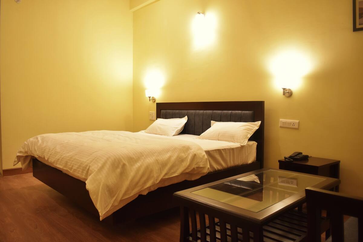 A hotel room with a bed, bedside lamps, a bedside table, and a glass-top table.