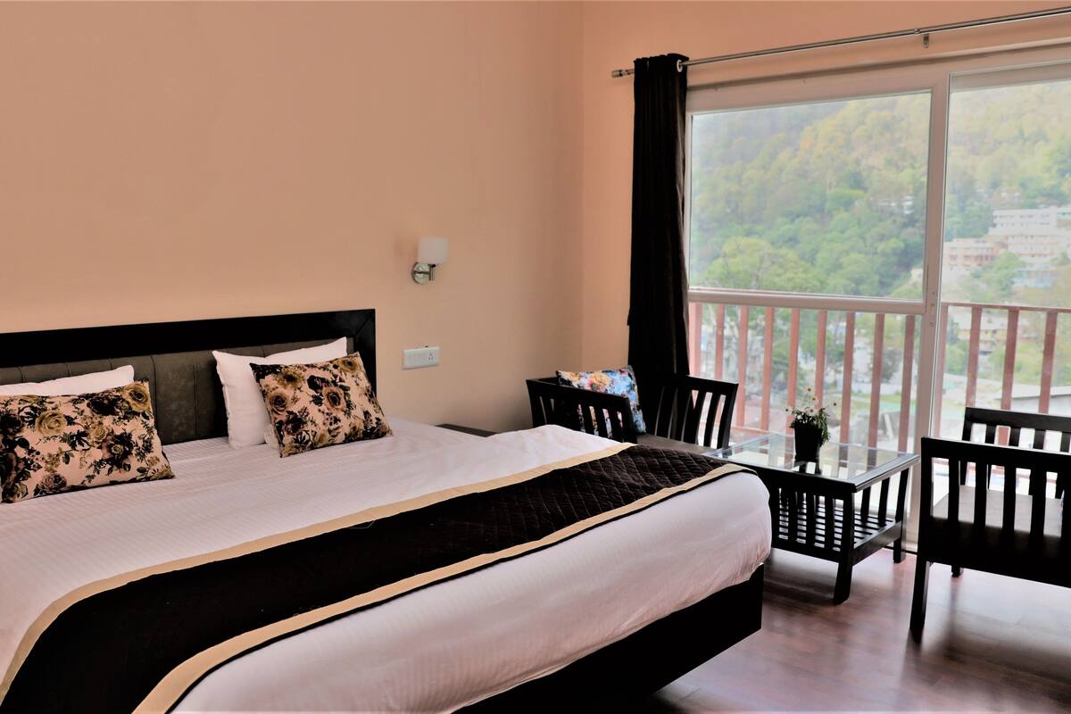 A bedroom with a large bed, a balcony with a view, and a small table with chairs.