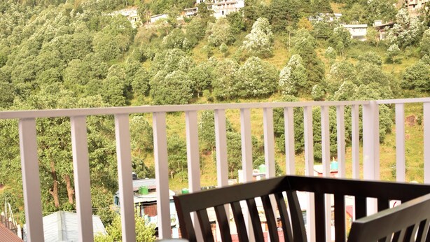 A balcony with a table and chairs, overlooking a hillside with houses and greenery. - Hotel Vista (Nainital)