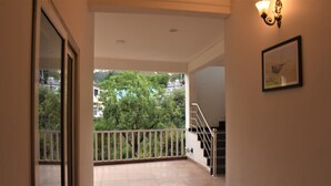 A corridor leading to a balcony with a view of trees and buildings. - Hotel Vista (Nainital)