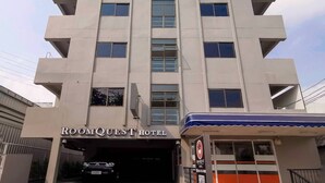 A multi-story hotel with a modern architectural design, featuring a prominent entrance and a sign that reads "ROOMQUEST HOTEL".