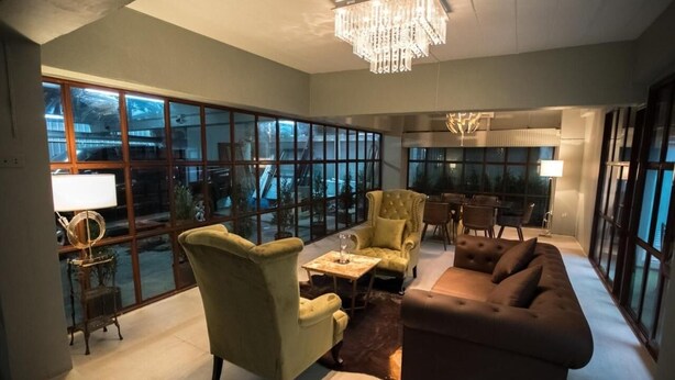 A spacious living room with a large window, a chandelier, and a brown sofa.
