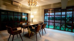 A modern dining area with a rectangular table, six chairs, a floor lamp, and large windows with a view of the outdoors.