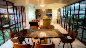A spacious dining area with a large marble table and modern chairs, large windows offering views of the outdoors, and a chandelier above.