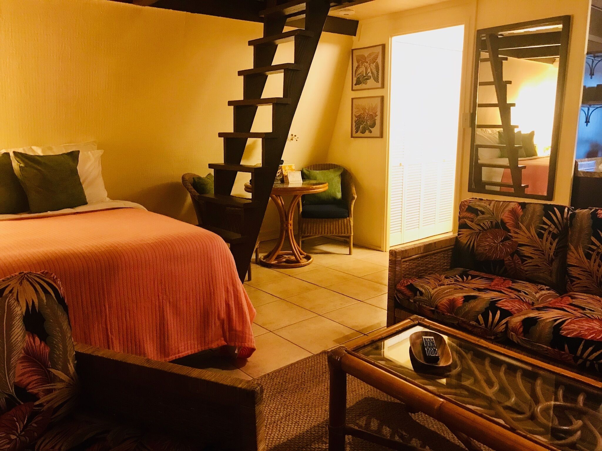 A bedroom with a bed, a chair, a sofa, a table, and a staircase.