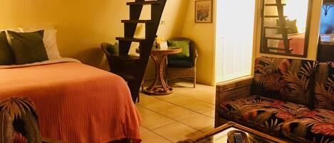 A bedroom with a bed, a chair, a sofa, a table, and a staircase.