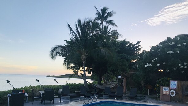 A pool area with lounge chairs and a view of the ocean at sunset.